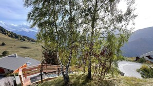 A rural setting with a wooden bridge, a building with a sloped roof, and a mountainous backdrop.