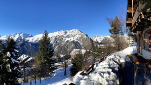 A mountain cabin with a wooden deck, snow-covered surroundings, and a clear view of the surrounding mountains.
