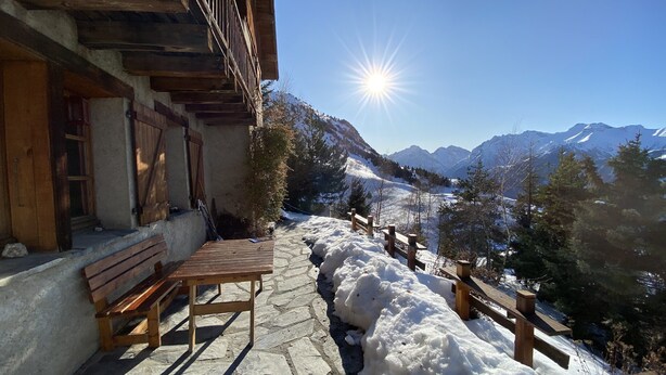 A wooden bench and table outside a building with a mountain view.