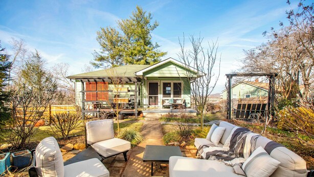 Uma casa com fachada verde, um pátio com móveis de exterior e um jardim.