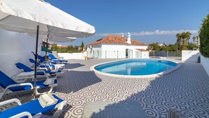 Un área junto a la piscina con sillones de descanso, una sombrilla blanca y una pileta.