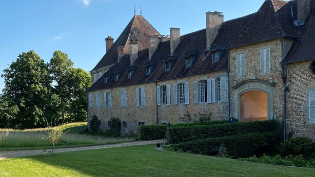 Un grand bâtiment en pierre, doté de nombreuses cheminées et d’une pelouse bien entretenue.