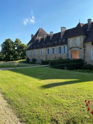Un grand bâtiment en pierre, doté de nombreuses cheminées et d’une pelouse bien entretenue.