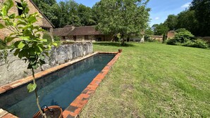 Une piscine rectangulaire bordée de briques, entourée d’une pelouse verdoyante et d’un mur de pierre.