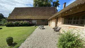 Un sentier de gravier mène à un bâtiment rustique doté d’un toit de chaume et de murs en briques.