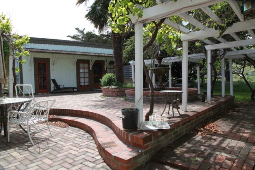 A covered patio area with brick flooring, white metal chairs, and a small table.