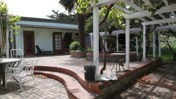 A covered patio area with brick flooring, white metal chairs, and a small table.