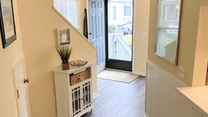 Un pasillo con suelo de madera, un armario blanco con puertas de cristal, un tapete verde estampado y una puerta que da al exterior.