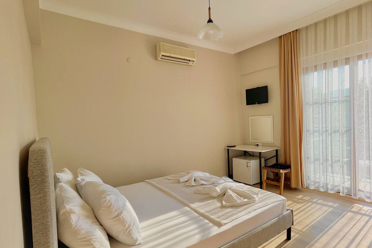 A hotel room with a bed, a desk, an air conditioner, a TV, and a window with curtains.