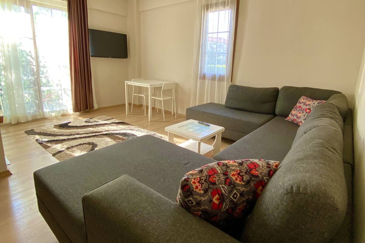 A modern living room with a grey sofa, a small white table, and a patterned throw pillow.