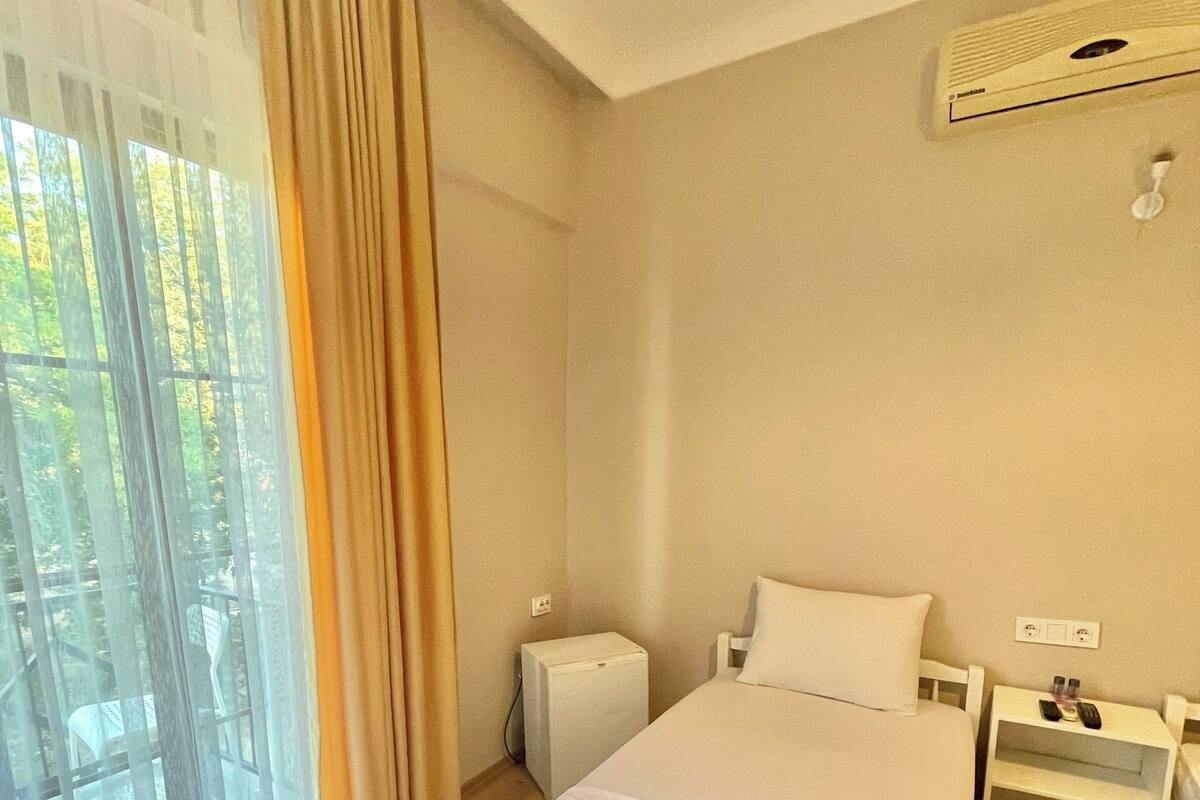 A hotel room with a bed, a nightstand, a window with curtains, and an air conditioning unit.