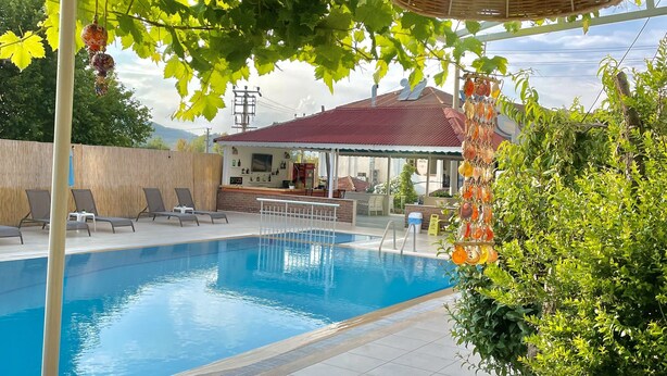 A swimming pool with lounge chairs, a pergola with hanging lights, and potted plants. - Cennet Hotel (Fethiye)
