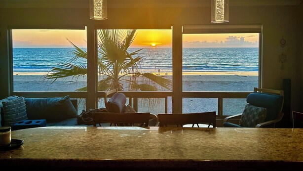 Una habitación con vistas al océano al atardecer, una zona de bar y una mesa de comedor.