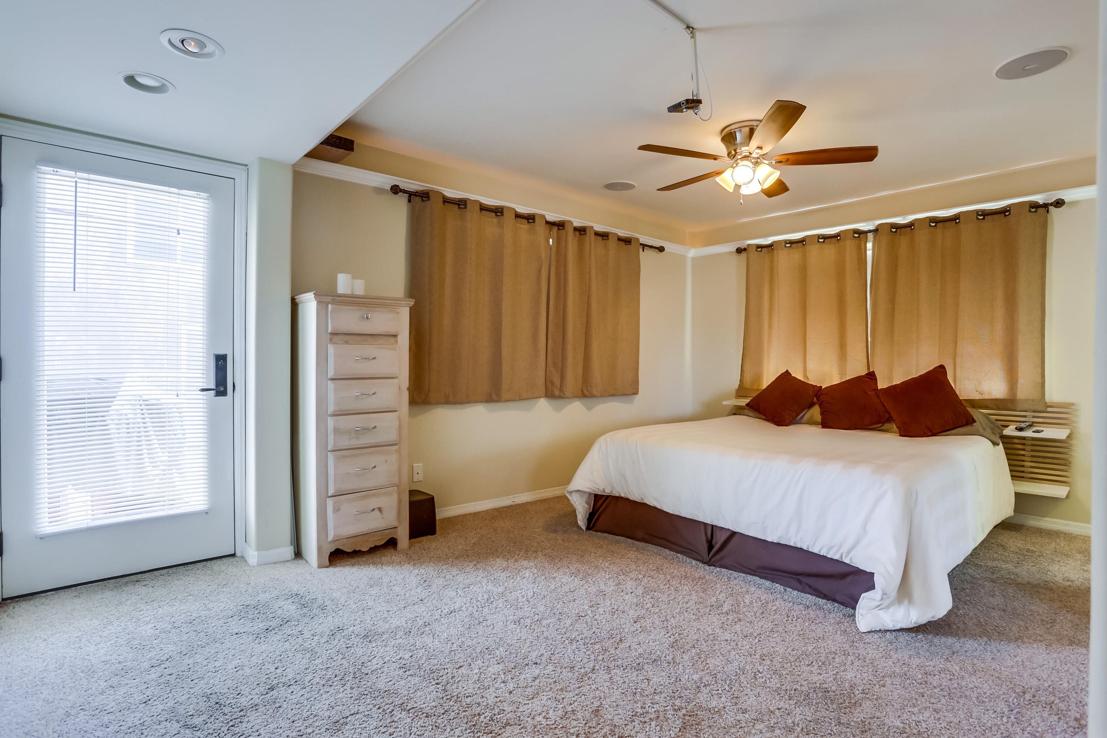 A bedroom with a bed, a dresser, a ceiling fan, and a window with curtains.