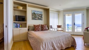 Un dormitorio con una cama grande, un televisor en un estante, un cuadro en la pared y un balcón con vistas.