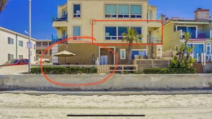 Un edificio de varios pisos con balcones, una playa arenosa al frente y un cielo azul despejado.