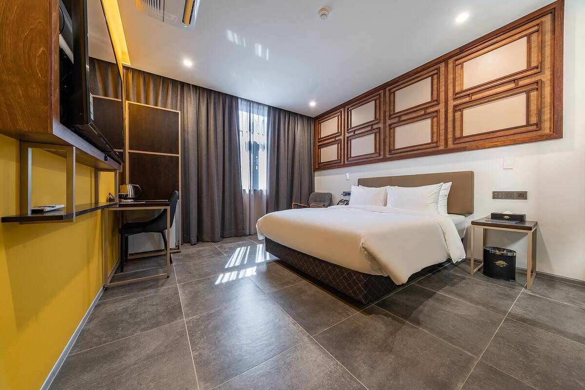 A modern hotel room with a large bed, a desk, and a built-in wardrobe.