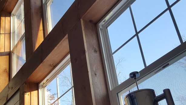 A room with wooden beams and large windows, a coffee maker, and a cup on a wooden ledge. - River Run: Secluded Riverside A-Frame & Sauna Two Miles West Of Grand Marais (Grand Marais)