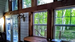 A wooden cabin interior with large windows, a dining table, and a chair. - River Run: Secluded Riverside A-Frame & Sauna Two Miles West Of Grand Marais (Grand Marais)