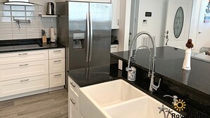 A modern kitchen with white cabinets, a stainless steel refrigerator, a black countertop, and a sink with a faucet.