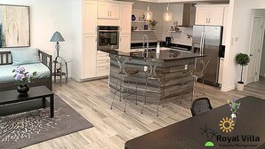 A modern kitchen with white cabinets, a central island with bar stools, a ceiling fan, and a dining area with a table and chairs.