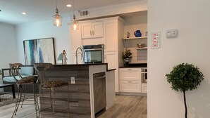 A modern kitchen with white cabinets, a central island with stools, and a potted plant.