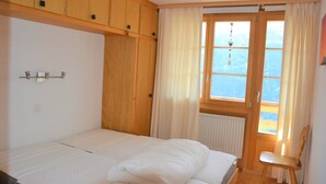 Een slaapkamer met een bed, houten kasten, een raam met gordijnen en een radiator.