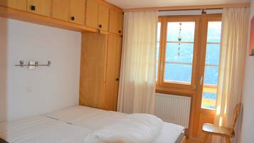 Une chambre à coucher avec un lit, des armoires en bois, une fenêtre avec des rideaux et un radiateur.