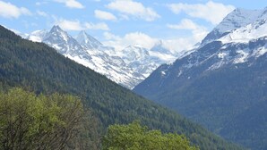 Een berglandschap met besneeuwde toppen en weelderige beboste valleien.