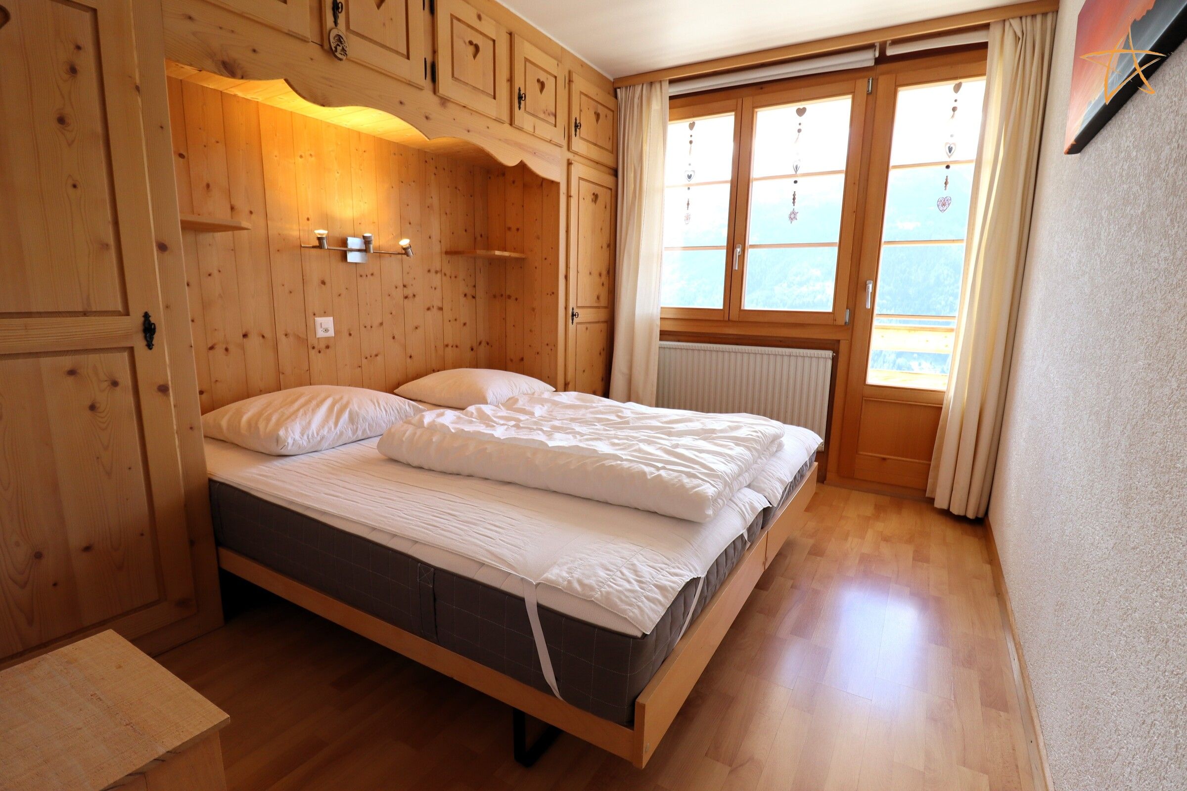 Ein Schlafzimmer mit Holzboden, einem Bett, Einbauschränken und einem Fenster mit Vorhängen.