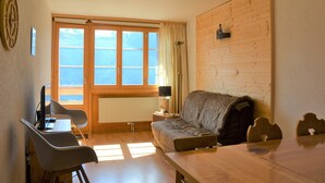 Een kamer met een houten tafel, twee stoelen, een bank, een lamp en een klok aan de muur.