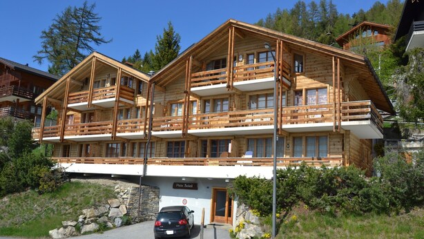 Een meerlaags houten chalet met balkons, een oprit van natuursteen en een auto ervoor.