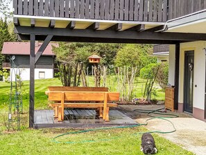 A wooden bench under a covered patio area with a garden and a house in the background. - Am Hohen Bogen by Interhome (Arrach)