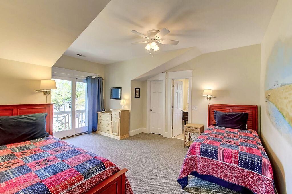 A bedroom with two beds, a ceiling fan, a dresser, and a television.