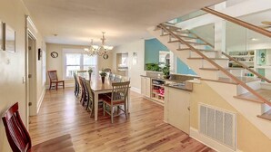 Un comedor amplio con una mesa y sillas de madera, un candelabro y una escalera que lleva a una zona de cocina.