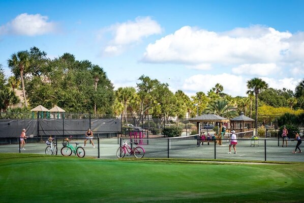 Una cancha de tenis con césped verde, una valla y árboles al fondo.