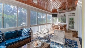 A covered porch with a wooden ceiling, wicker furniture, and large windows offering views of greenery. - 2602 Hartnett Boulevard (Isle of Palms)