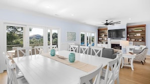 A spacious living room with a white dining table, white chairs, a fireplace, a TV, and a bookshelf. - 2307 Palm Boulevard (Isle of Palms)