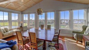 A spacious room with a large wooden table, comfortable seating, and large windows offering a view of the outdoors. - 21 Ocean Point (Isle of Palms)