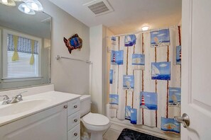 A bathroom with a white sink, a toilet, and a shower curtain with nautical-themed artwork. - 1010 Ocean Palms 201 (Isle of Palms)