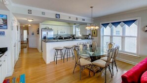 A modern kitchen with a central island, bar stools, and a dining table with chairs. - 1010 Ocean Palms 201 (Isle of Palms)