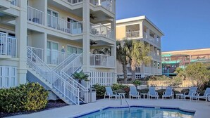 A multi-story hotel with balconies, a swimming pool, and lounge chairs. - 1010 Ocean Palms 201 (Isle of Palms)