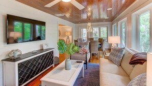 Een moderne woonkamer met een grote televisie, houten plafond en een gezellige zithoek met een bank en stoelen.