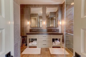 A modern bathroom with two sinks, large mirrors, and a glass shower enclosure.