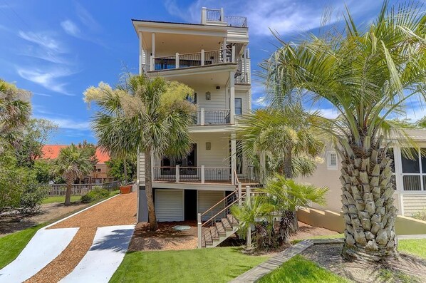 A multi-story residential building with a balcony on the upper floor, surrounded by palm trees and a well-maintained lawn.