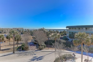 A hotel with a view of the ocean, surrounded by palm trees and a parking area.