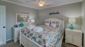 Ein Schlafzimmer mit Bett, Deckenventilator, Kommode, Nachttisch und spiegelt sich in einem an der Wand befestigten Spiegel wider.