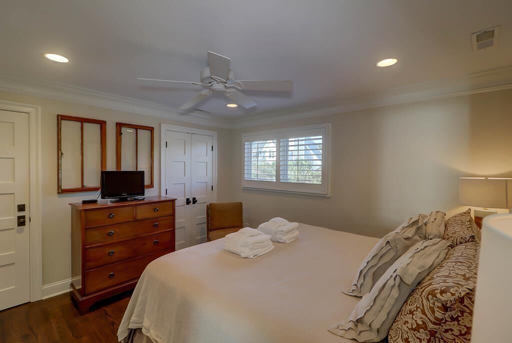 A bedroom with a bed, a dresser, a television, a ceiling fan, and a window with blinds.