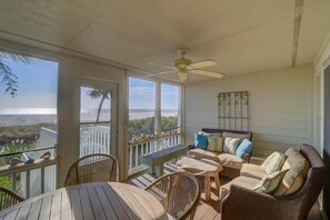 A covered outdoor seating area with a view of the ocean, a ceiling fan, and a wooden table.