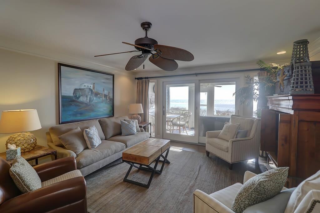 A spacious living room with a large painting, a ceiling fan, and a view of the ocean through large windows.